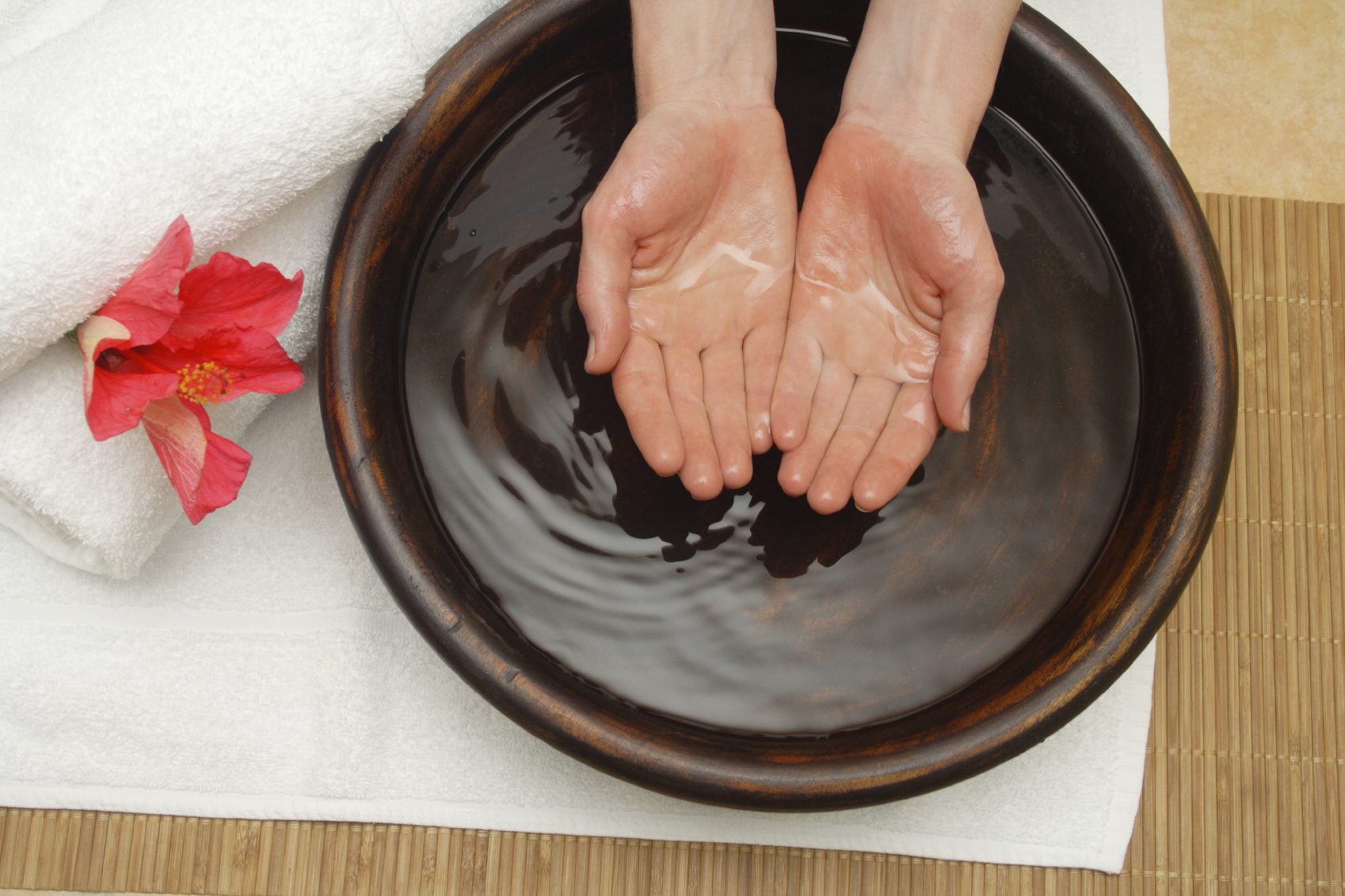 Two hands cupped in a bowl of water, with a towel and flower nearby.